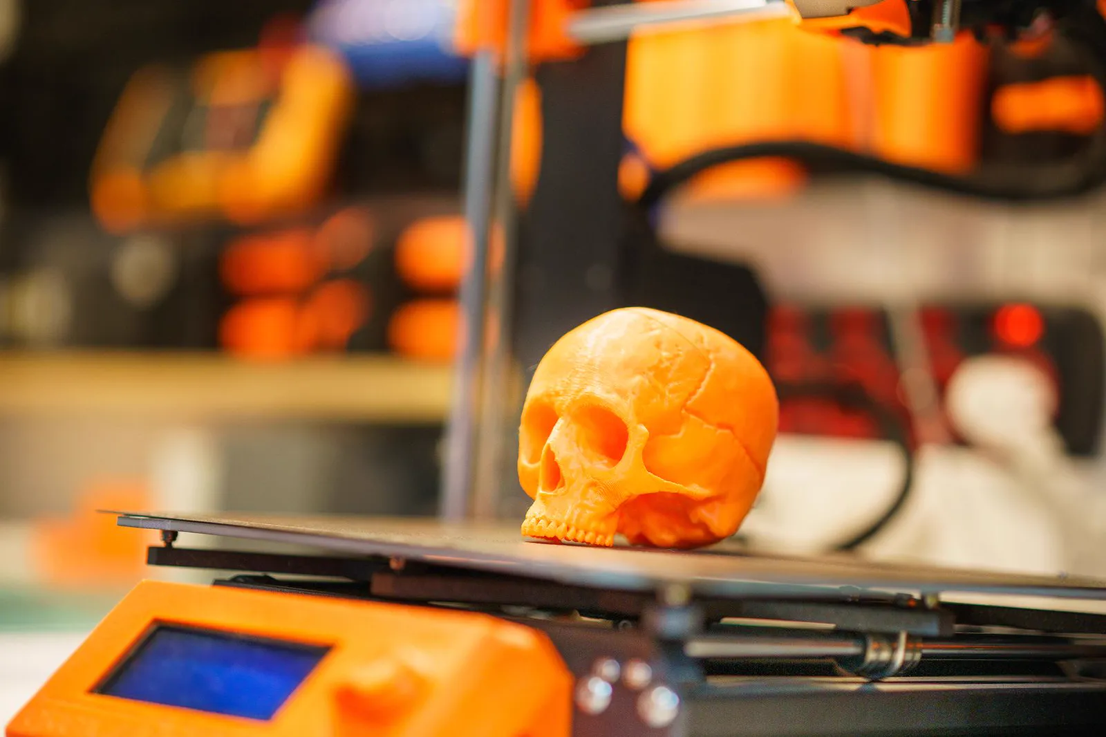 Caveira laranja recém-impressa sobre a mesa de uma impressora 3D em uma oficina