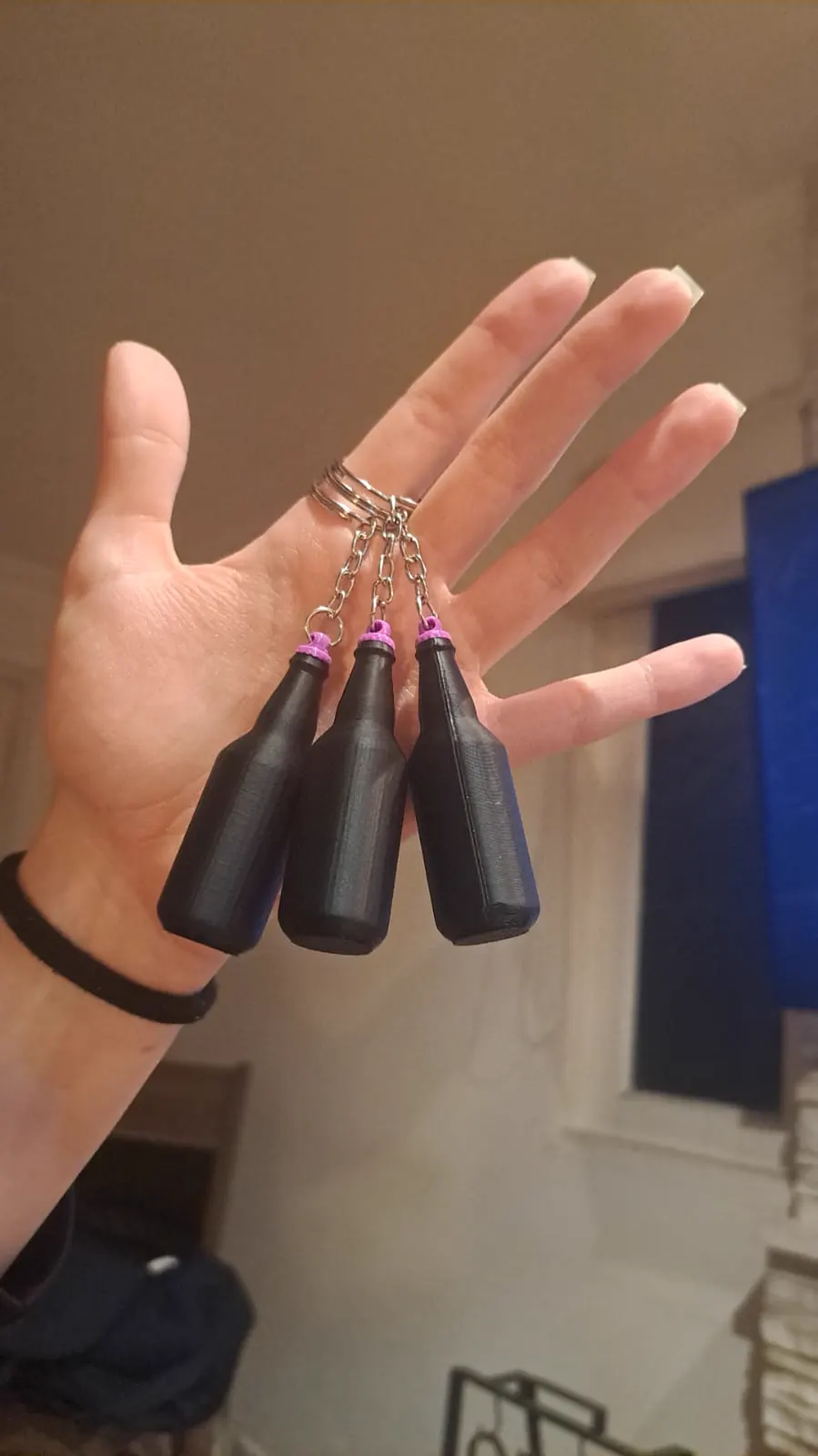 Mão segurando três chaveiros em forma de garrafinha preta